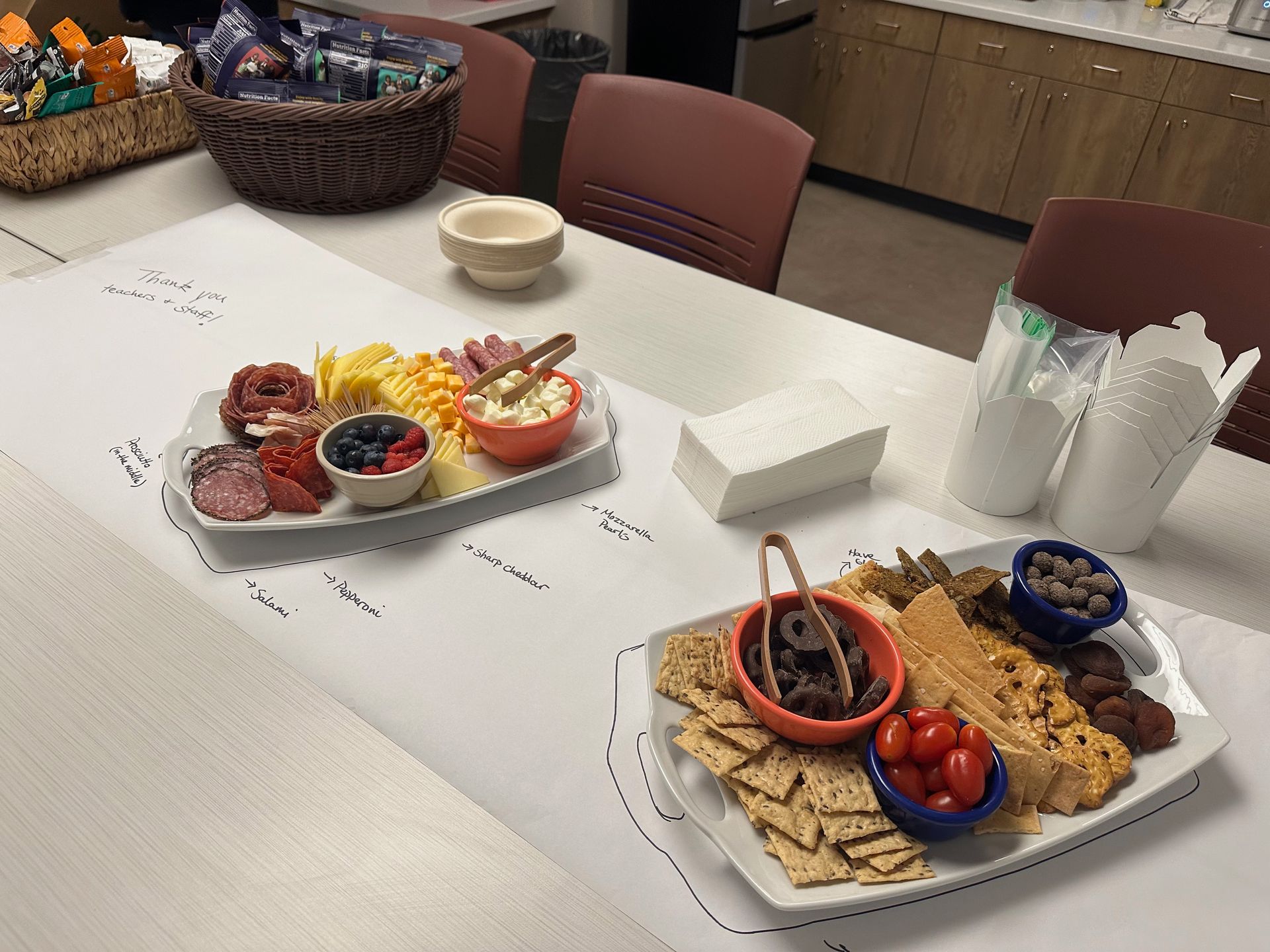 Two charcuterie boards on a table. One with meats and cheese, the other with crackers and olives.