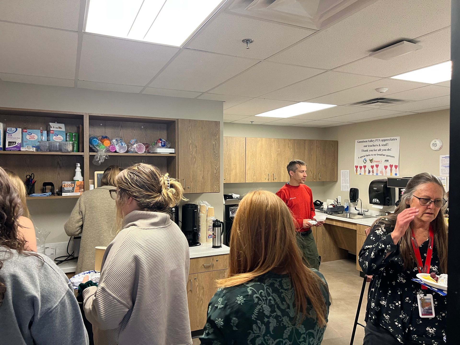 People gathered in a room with cabinets and lab equipment. A man in red shirt speaks, others listen.