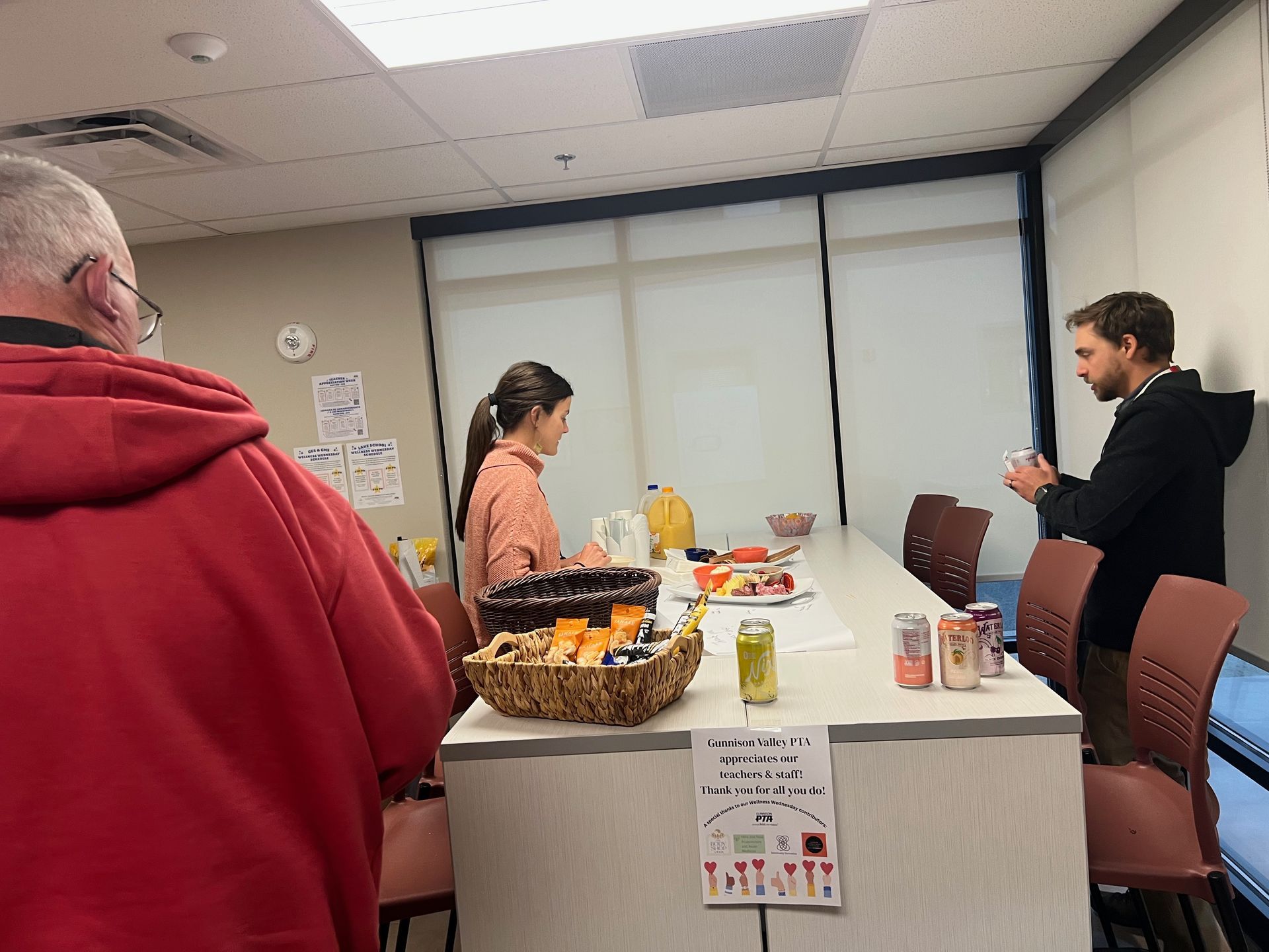People near a table with snacks and drinks in an office setting.