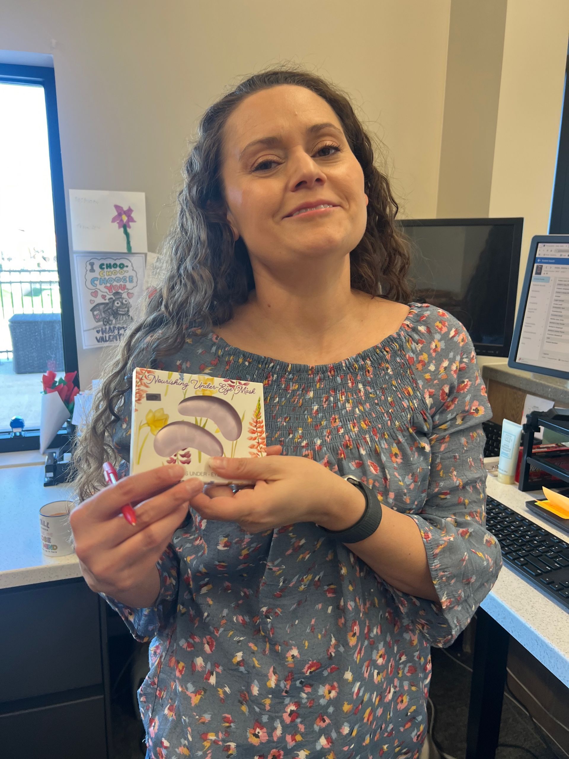 Woman holding a package with purple eye patches, smiling. Office setting.