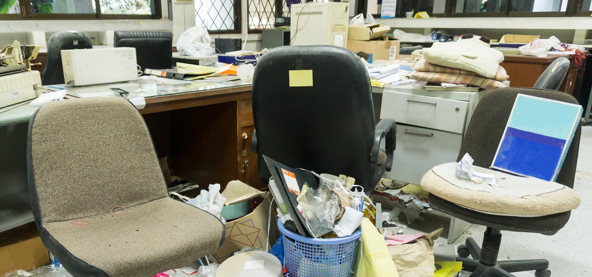 A cluttered office space with various discarded items, including papers, folders, and office supplie