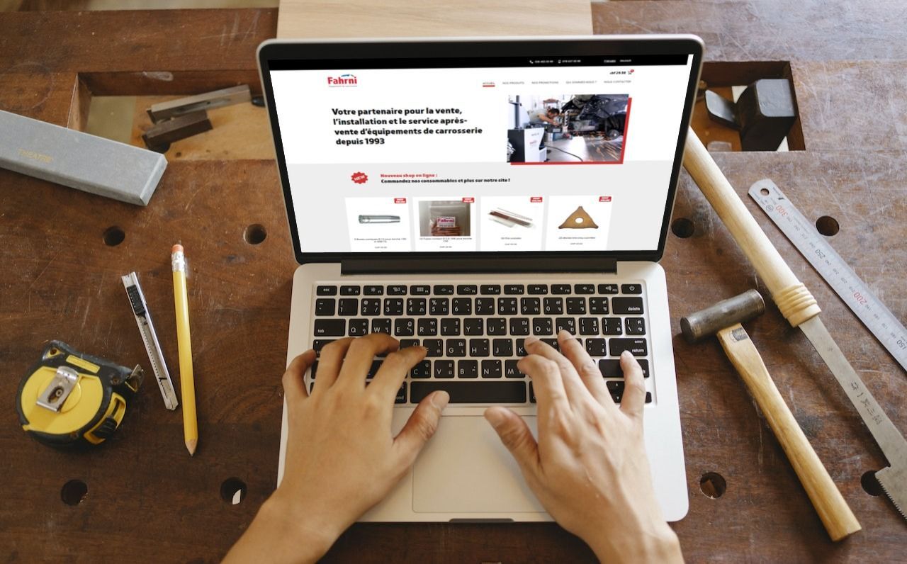 Une personne utilise un ordinateur portable sur un établi avec des outils, en train de consulter un site web.