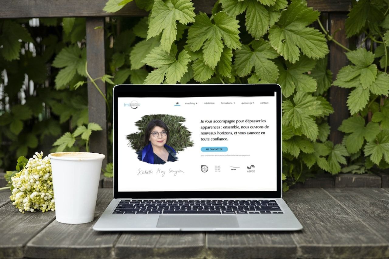Ordinateur portable affichant un site web avec le portrait d'une femme, une tasse de café et du feuillage.