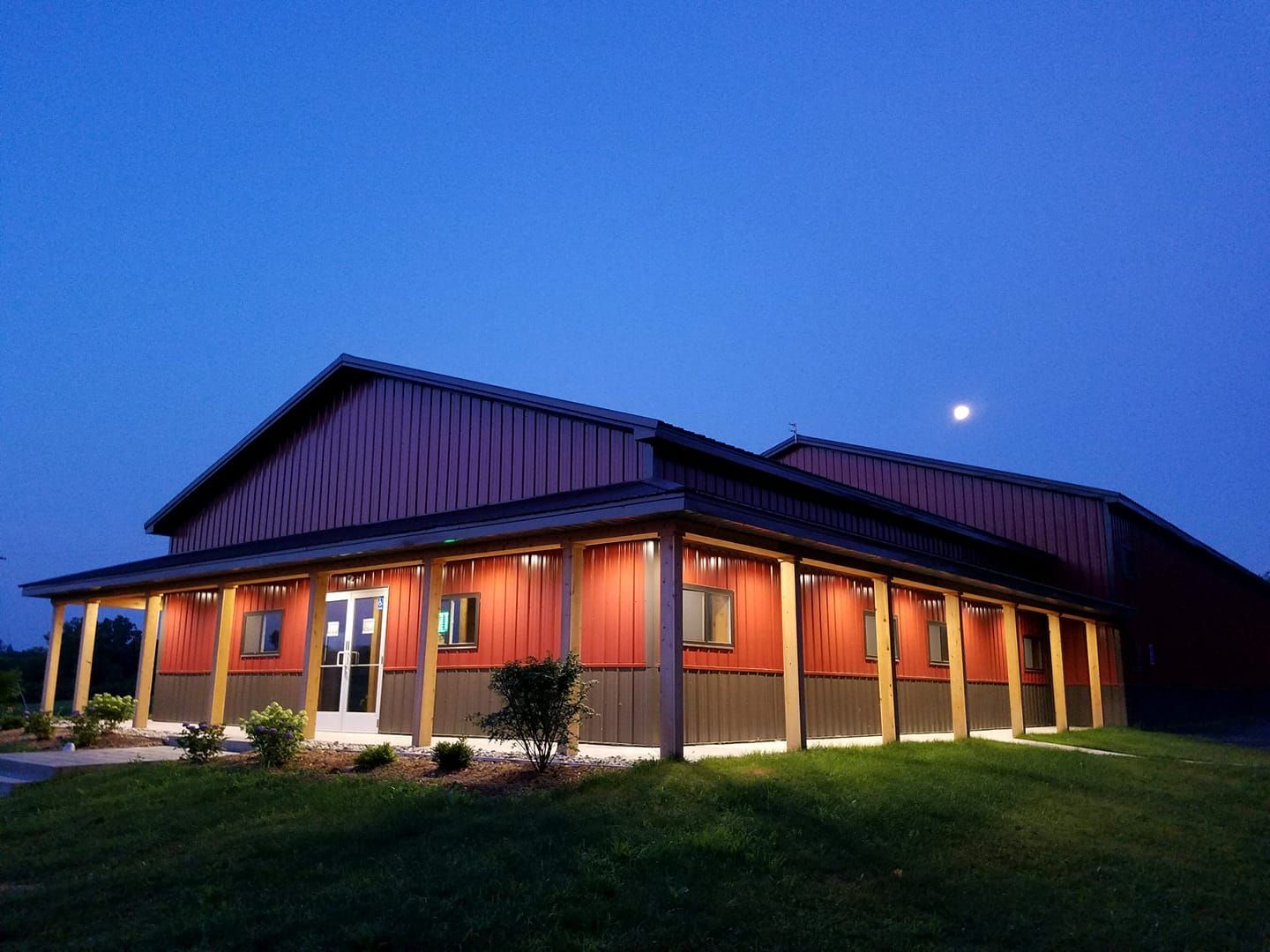 Building with red and gray siding, lit porch, under a dark blue sky with a moon.
