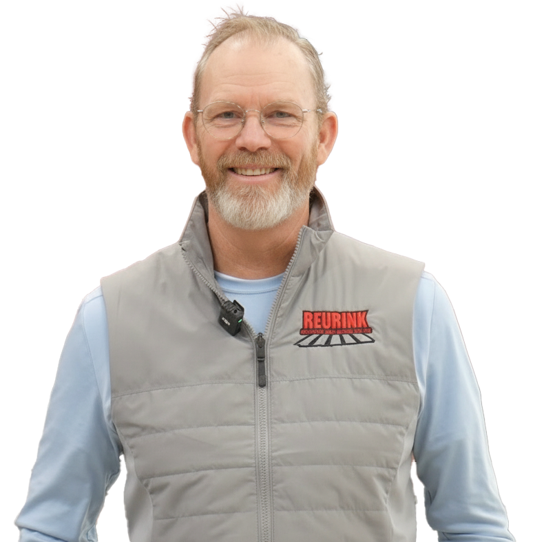 Man with glasses, gray vest, light blue shirt, smiling, REURINK logo on vest.