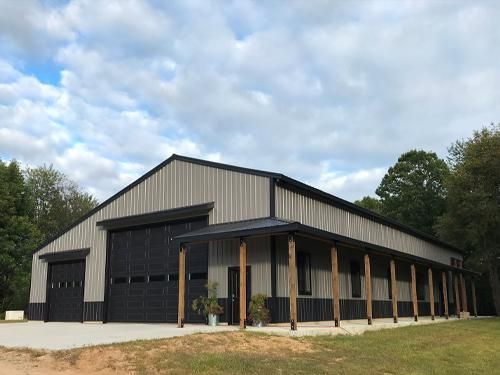 Large metal building with black accents and a covered porch. Light gray siding and a concrete foundation.