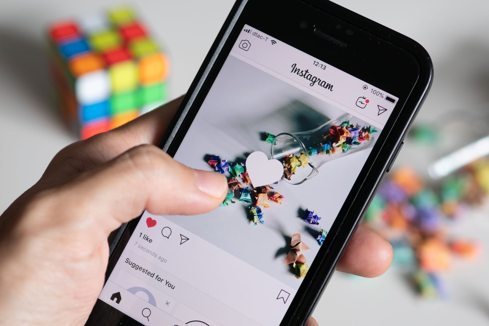 Hand holding a smartphone displaying colorful artwork, with a Rubik’s Cube in the background