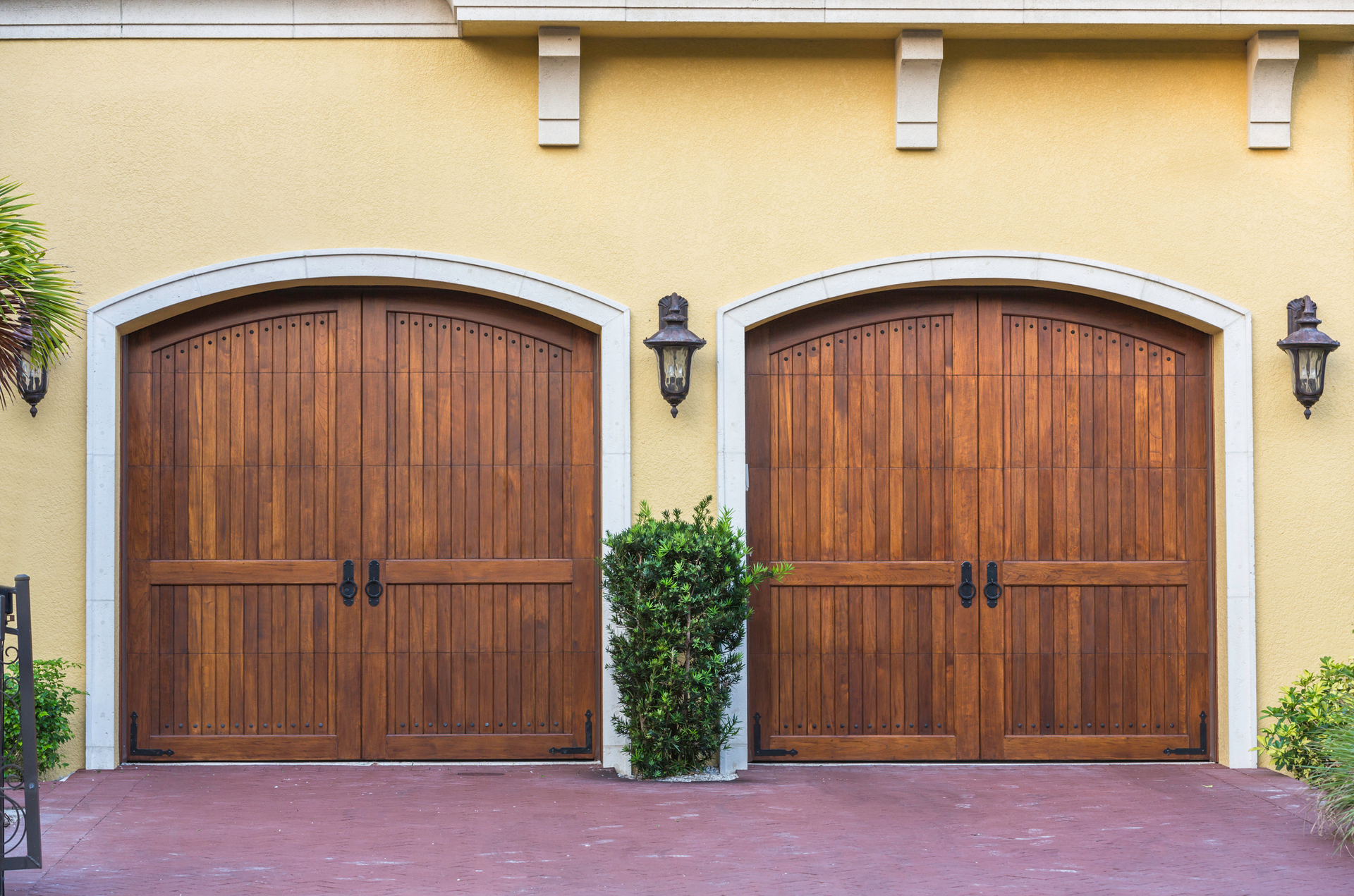 Two wooden garage doors with arch trim, on a yellow stucco building.
