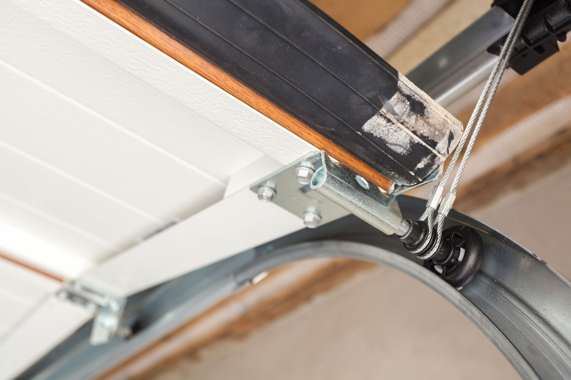 Close-up of a garage door track and mechanisms, showing the track, door, cable, and bracket.