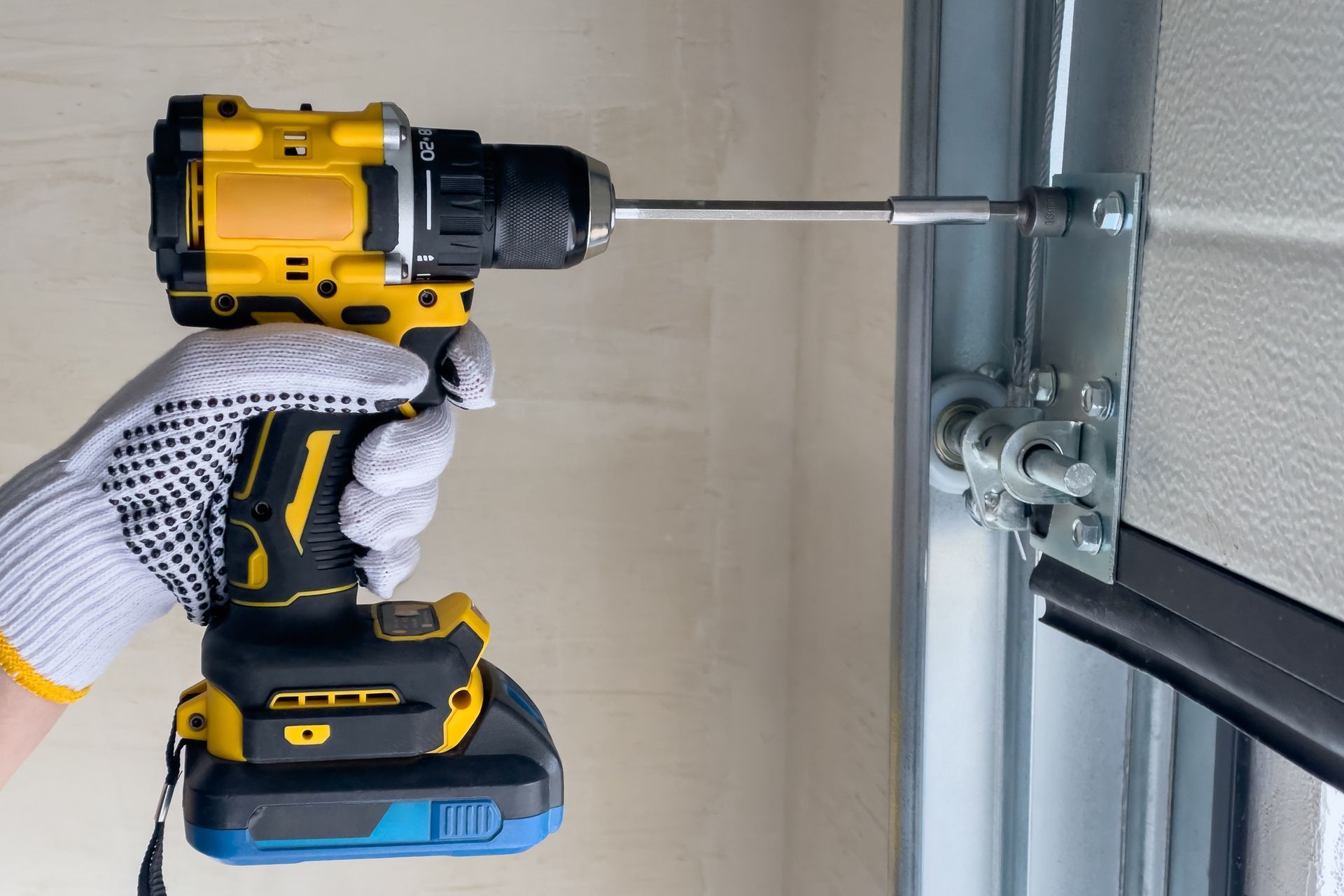 A person in work gloves using a yellow drill to secure a garage door bracket.