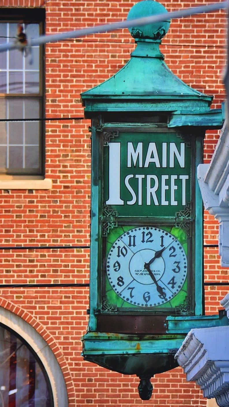 A clock hanging from a pole that says main street
