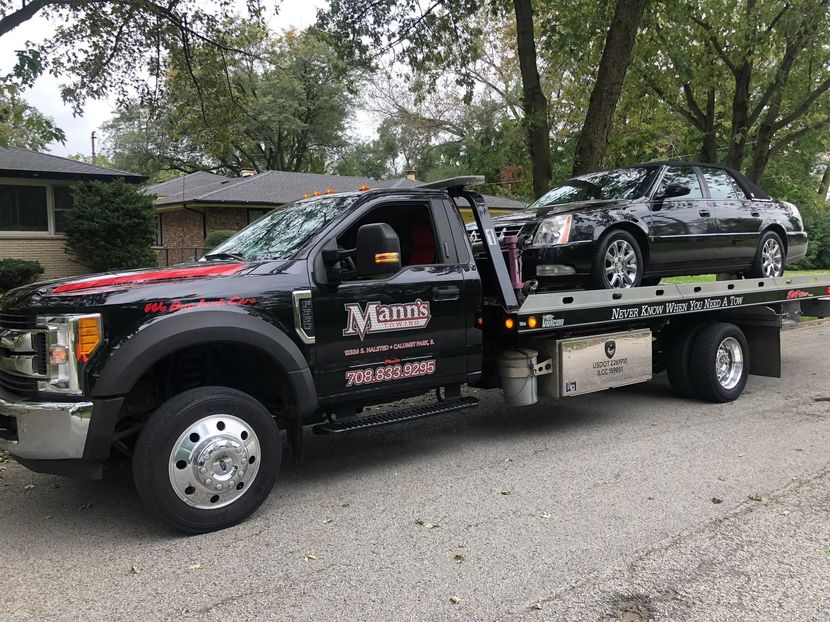Tow truck transporting a silver car on a flatbed in a residential neighborhood