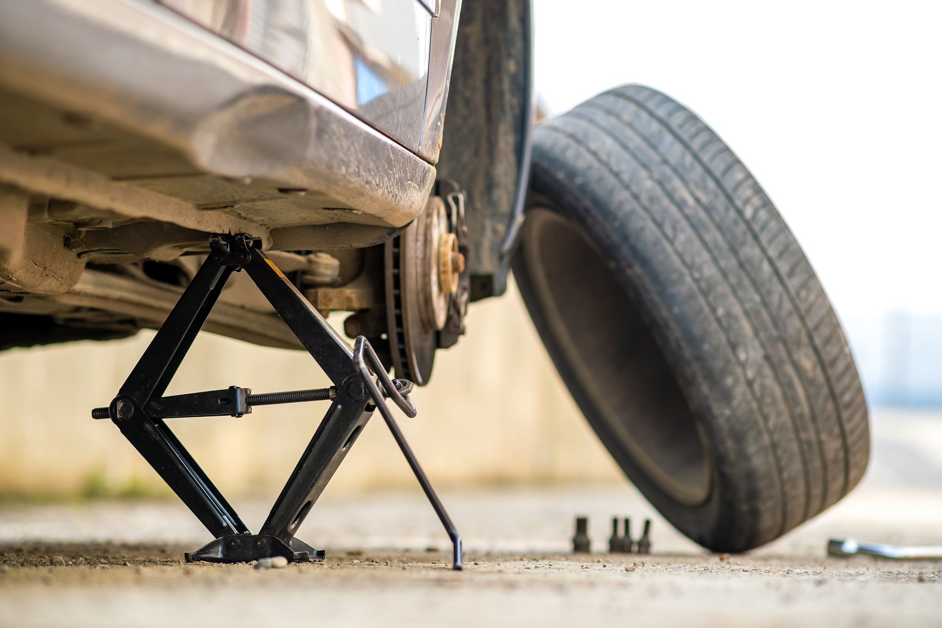 Car jack lifting a car with a detached wheel on the ground in a roadside repair scene