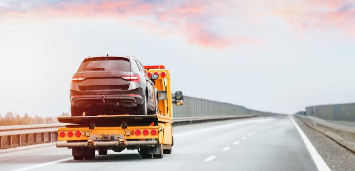 Tow truck hauling a black SUV on a highway under a cloudy sky