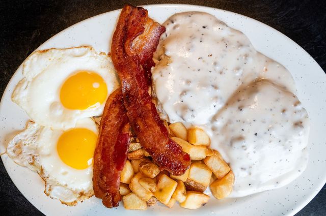 Breakfast plate with fried eggs, bacon, home fries, and white gravy on a white plate
