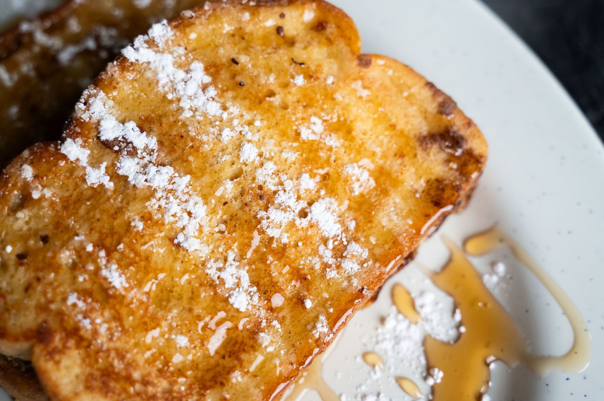 Powdered-sugar-dusted toasted bread on a white plate with syrup.