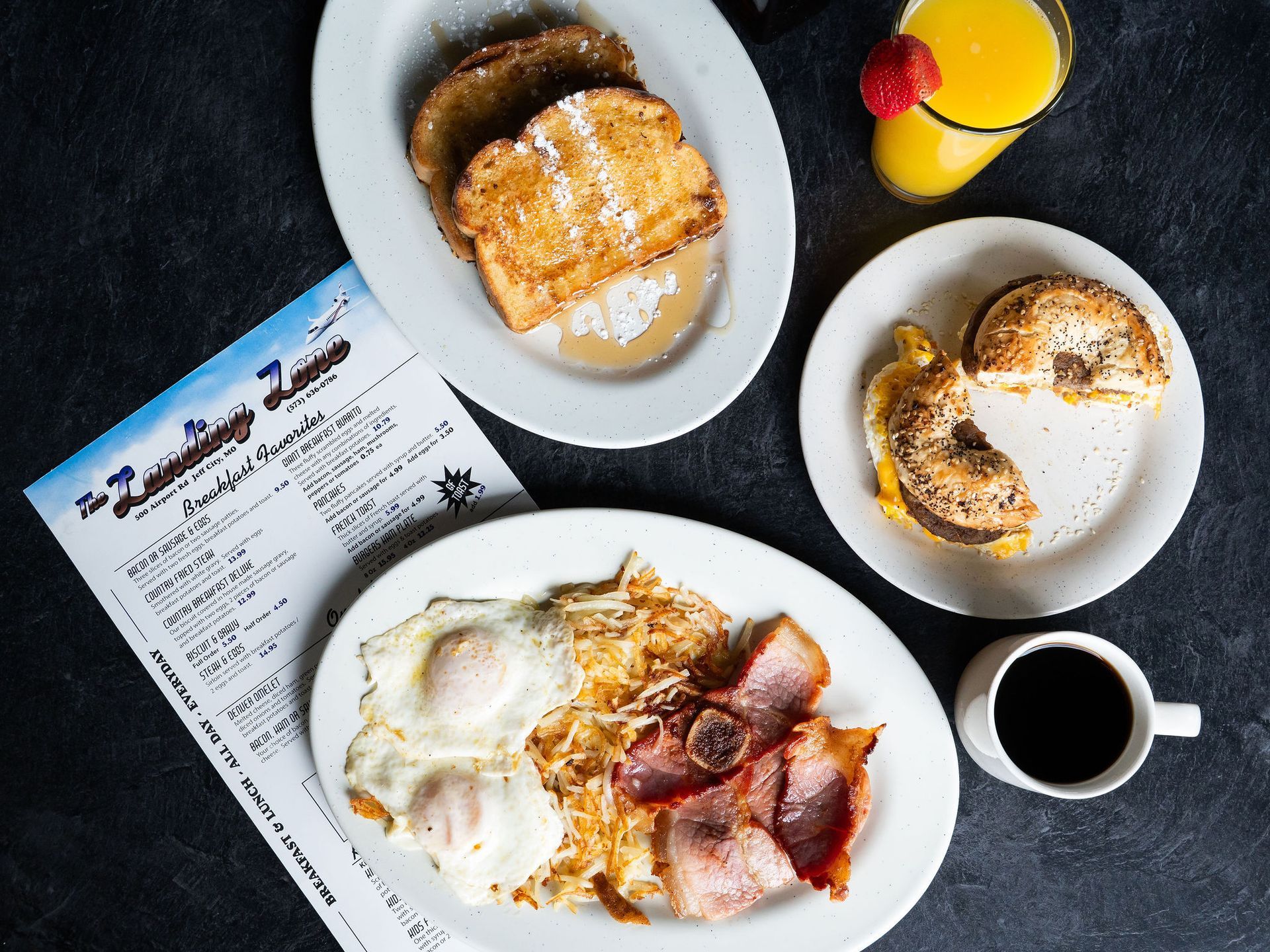 Breakfast spread with pastries, eggs, bacon, coffee, juice, and a menu on a dark table