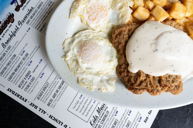 Breakfast plate with eggs, biscuits and gravy, potatoes, and a newspaper underneath