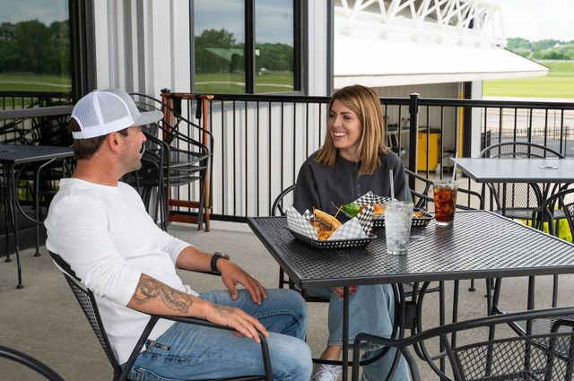 Two people chatting at an outdoor café table with drinks and food on a patio