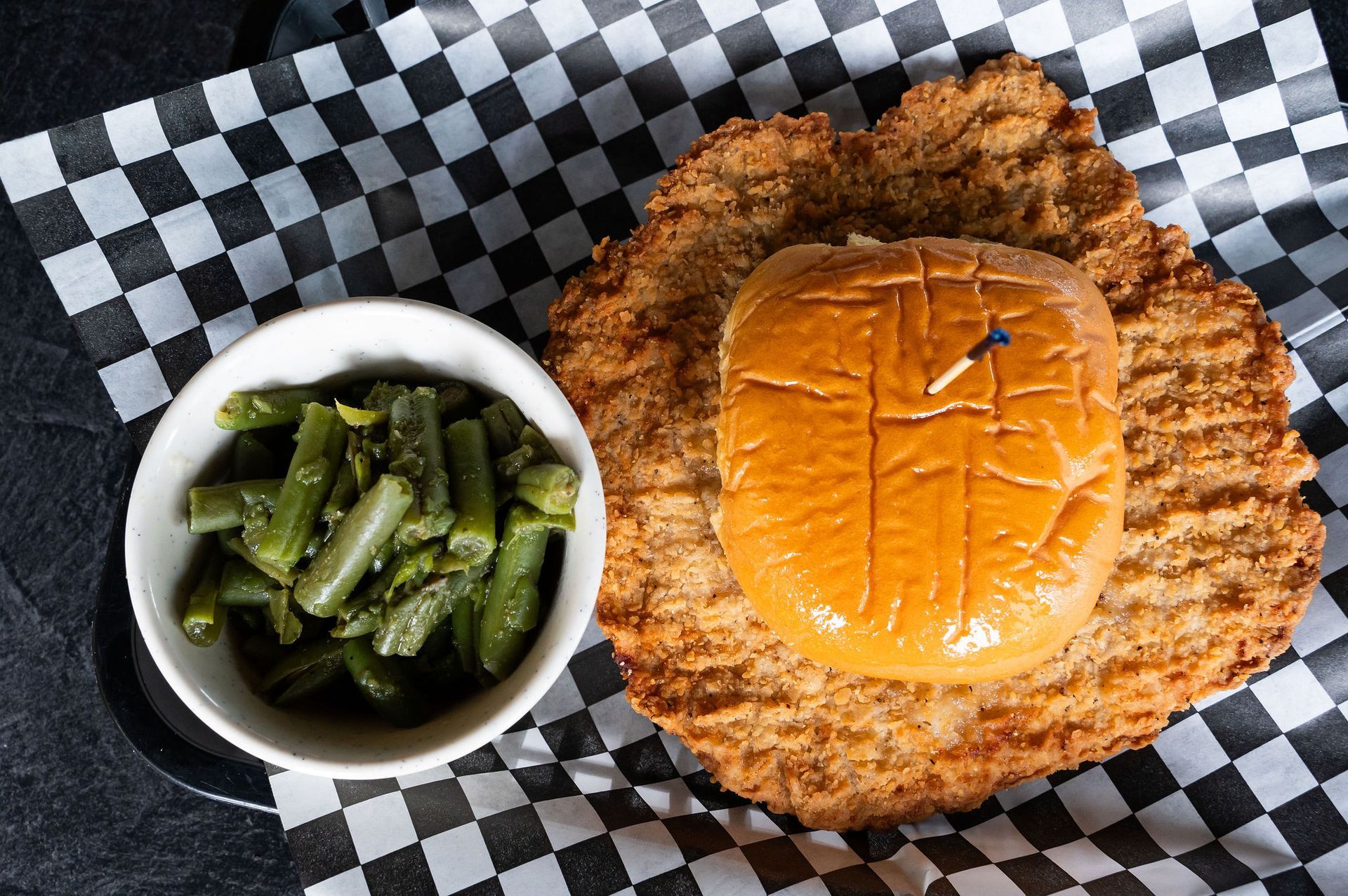 Fried chicken sandwich with pickles and a side of green beans on checkered paper