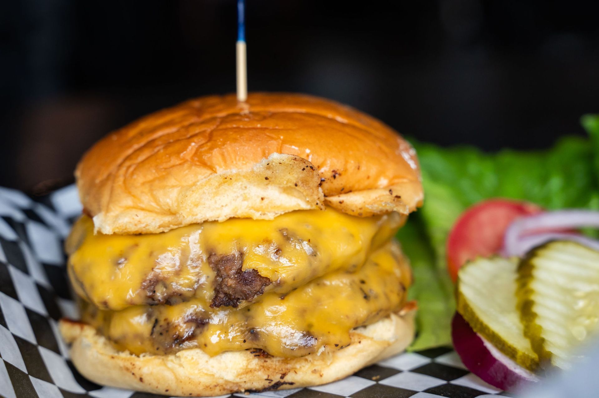 Cheeseburger with melted cheese, pickles, and lettuce on a checkered tray lining