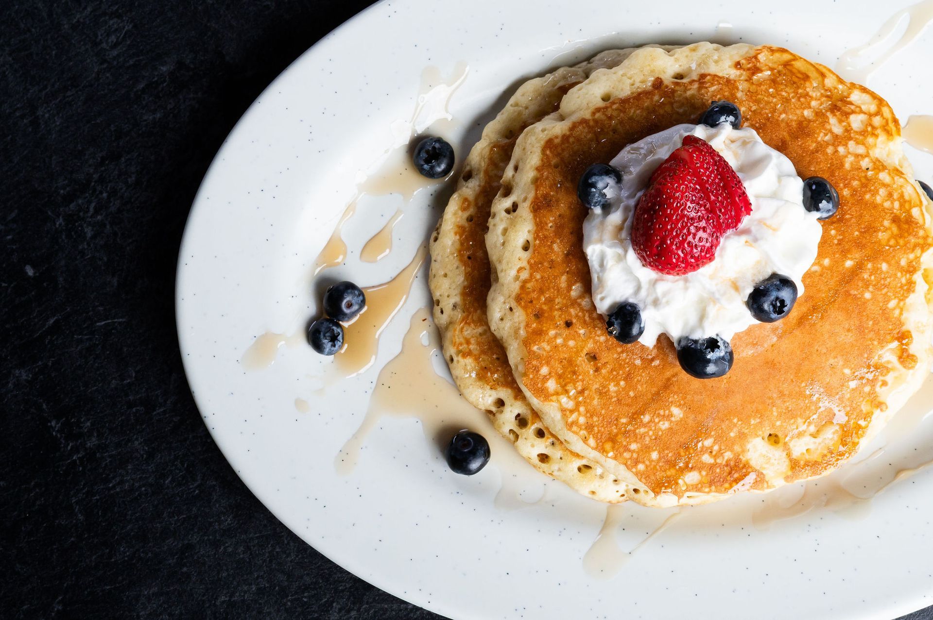 Pancakes topped with whipped cream, strawberries, and blueberries on a white plate.