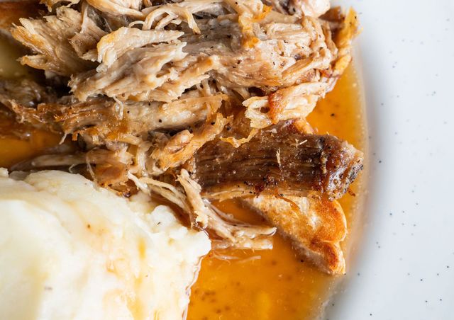 Shredded meat with mashed potatoes in orange gravy on a white plate