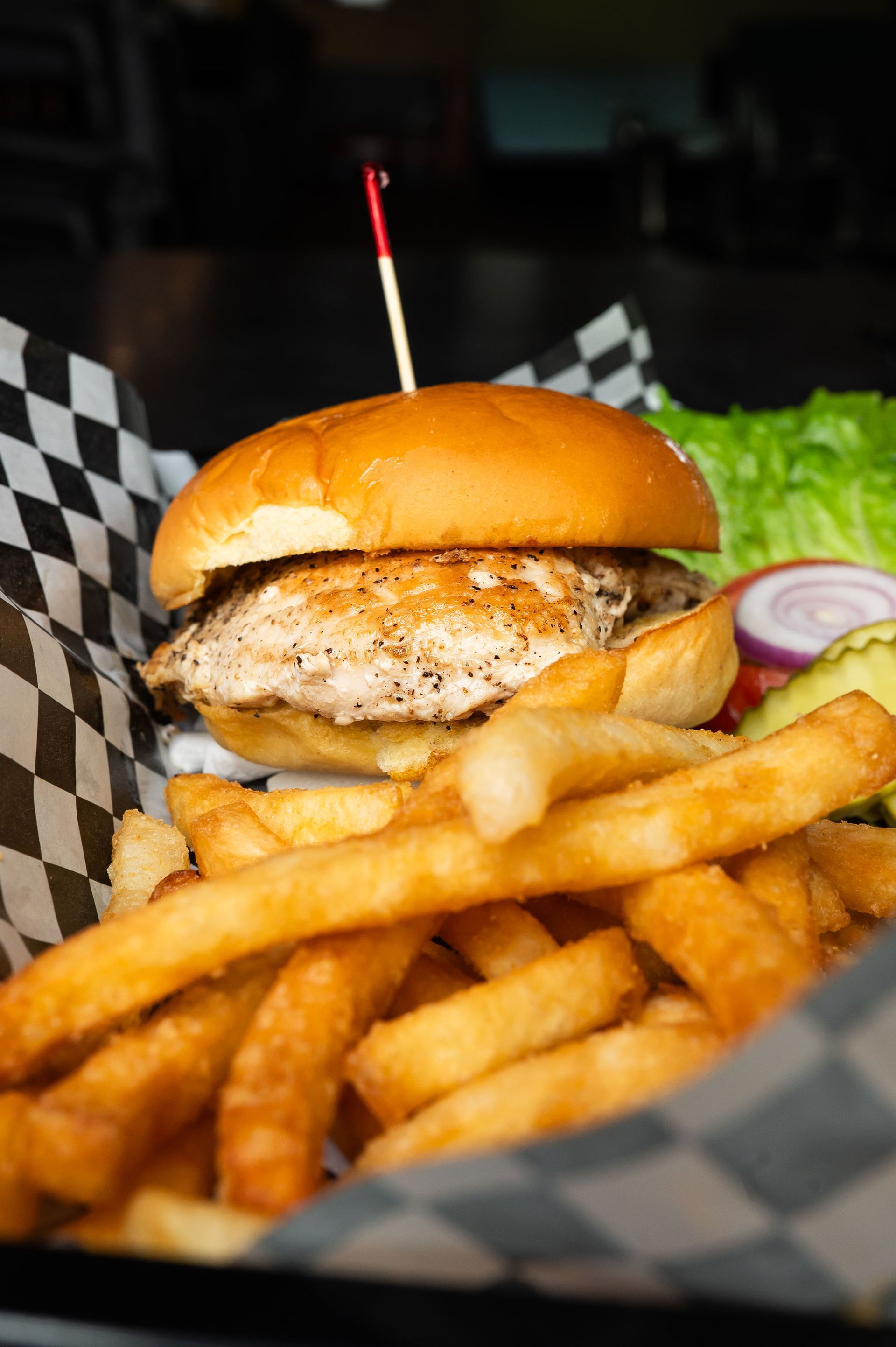 Burger and fries in a basket with black-and-white checkered paper, topped with a toothpick flag