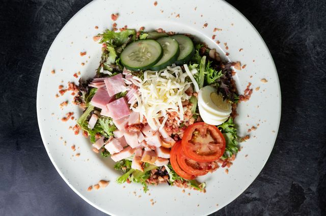 Colorful salad with ham, cucumber, tomato, cheese, and greens on a white plate