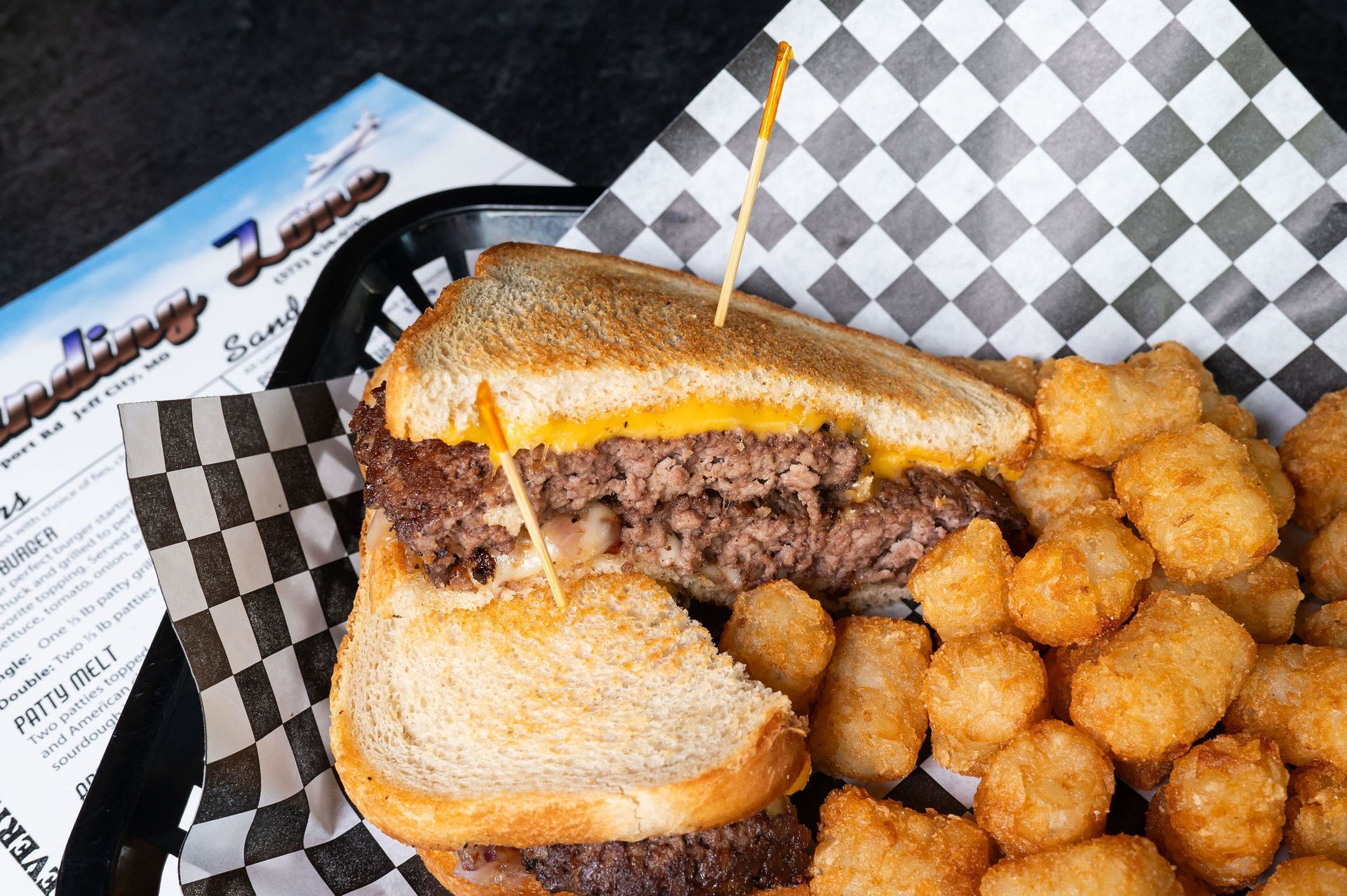 Cheeseburger sandwich with tater tots in a basket lined with black-and-white checkered paper