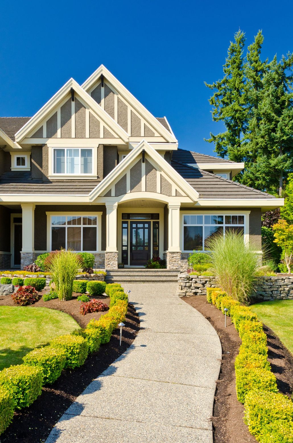 Modern gray house with a stone walkway, manicured garden, and blue sky