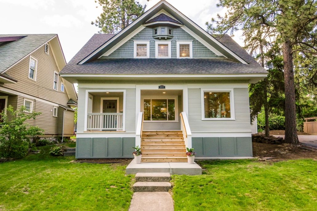 Front view of a blue-gray bungalow with a porch, front steps, and green lawn