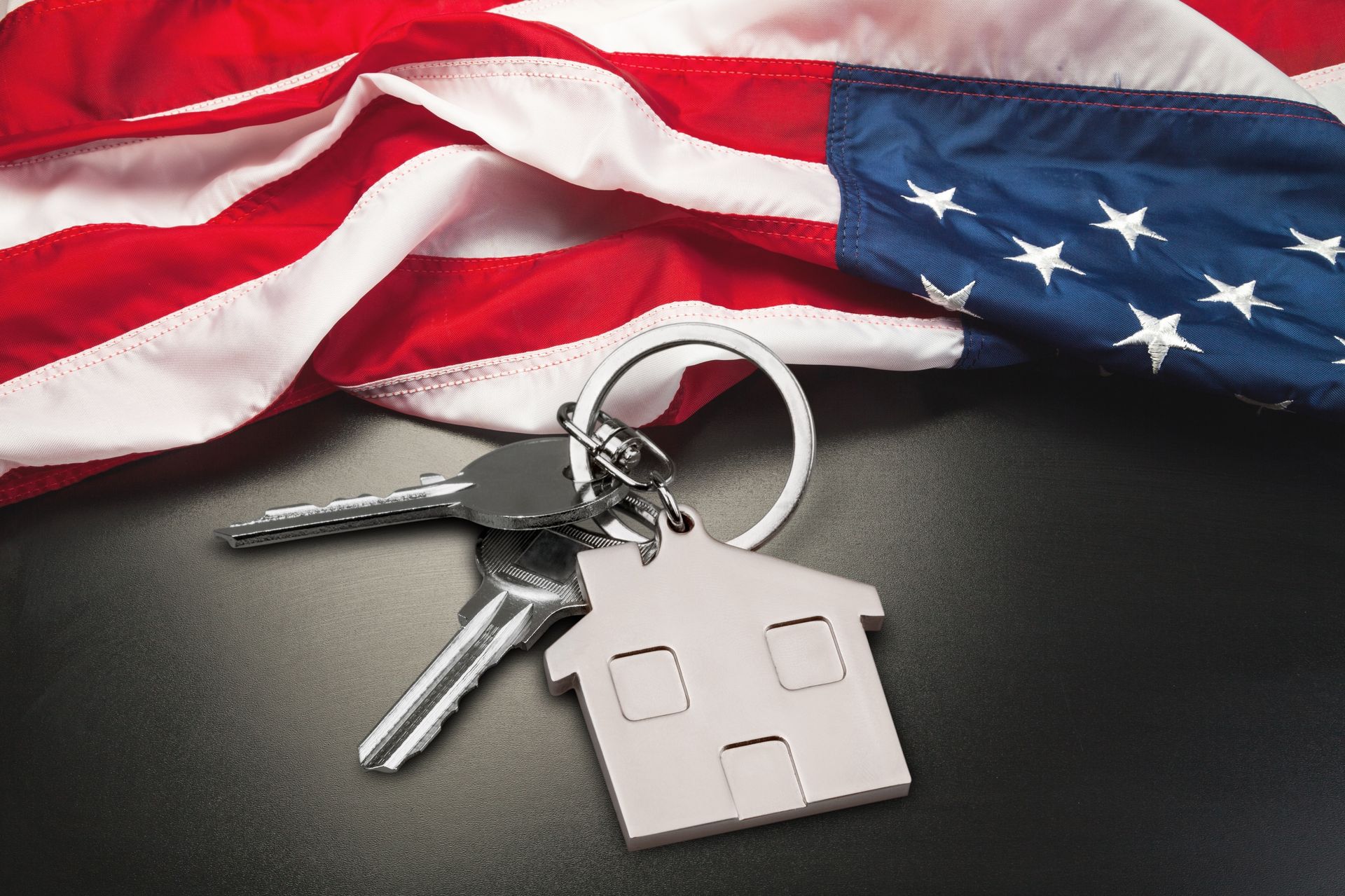 American flag with house-shaped keychain and keys on a dark surface