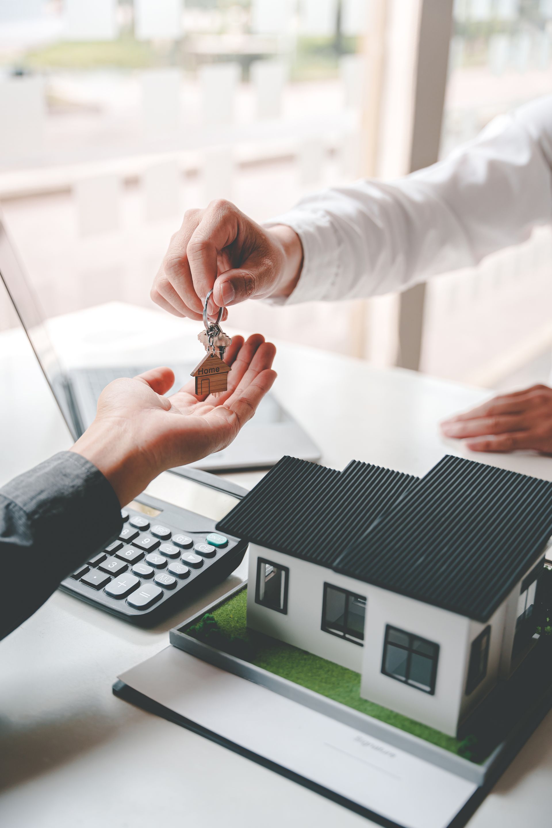 Keys handed over at a house model with calculator, symbolizing a real estate sale