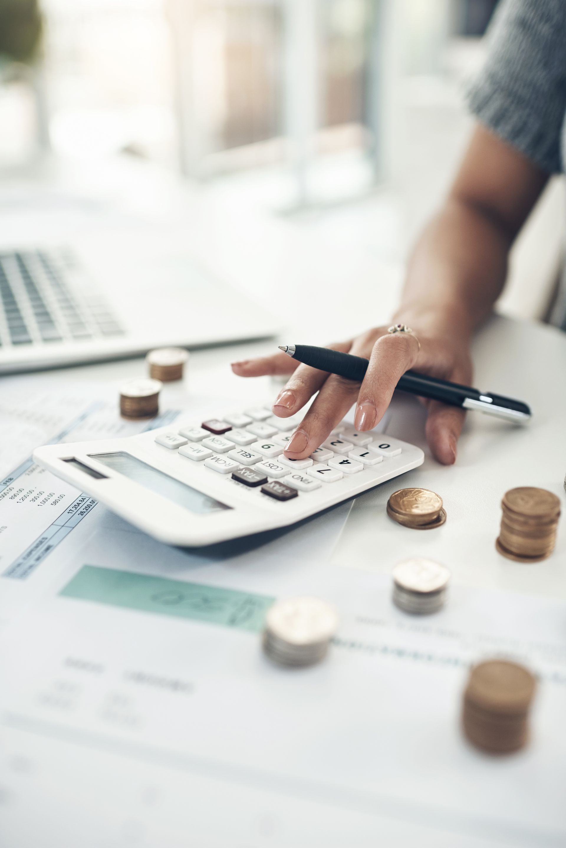 Hand using a calculator beside scattered coins and bills on a desk
