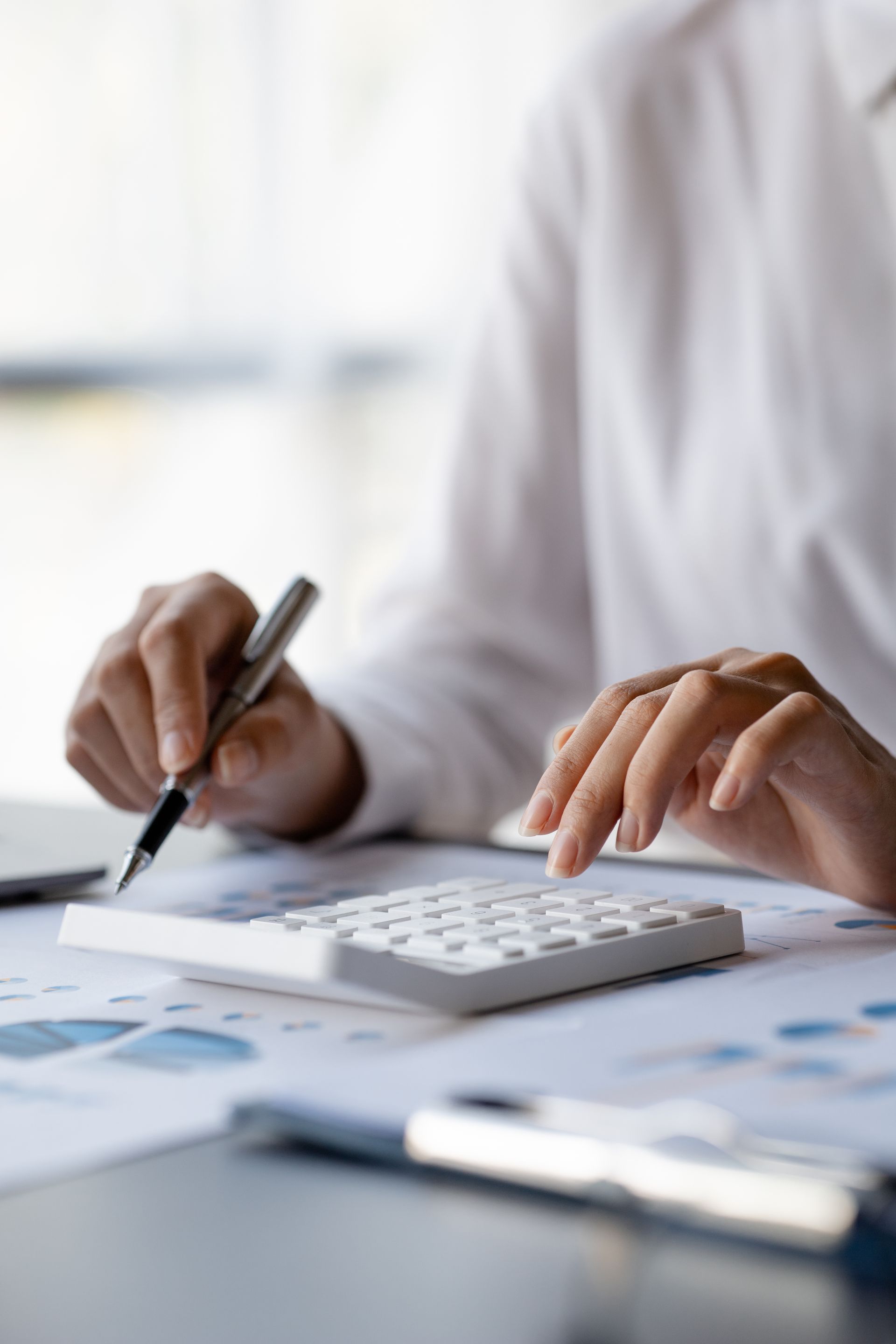 Hands using a calculator and pen over financial documents on a desk