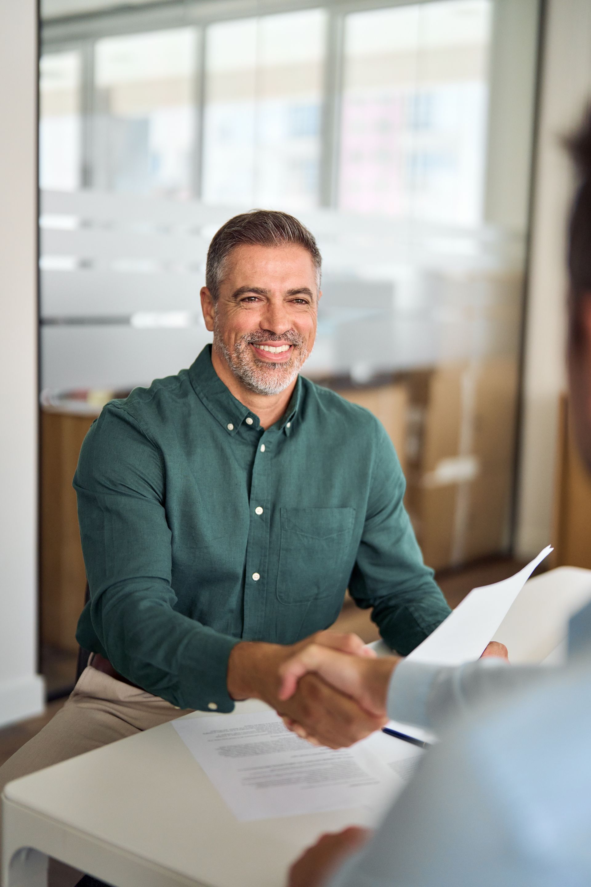 Two people smiling and shaking hands with a realtor in a bright living room