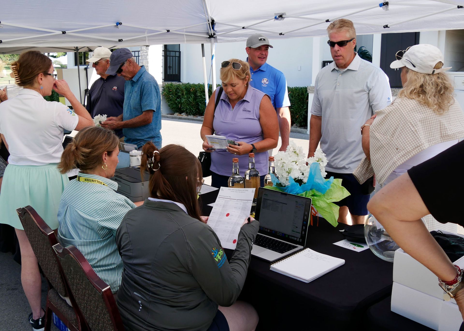 VIPS staff sitting at a table signing in golfers. Golfers are standing on the other side wait to register.