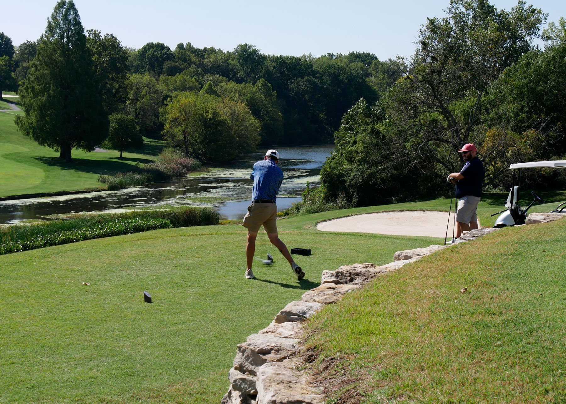 Two male golfers, one teeing off while other watches.