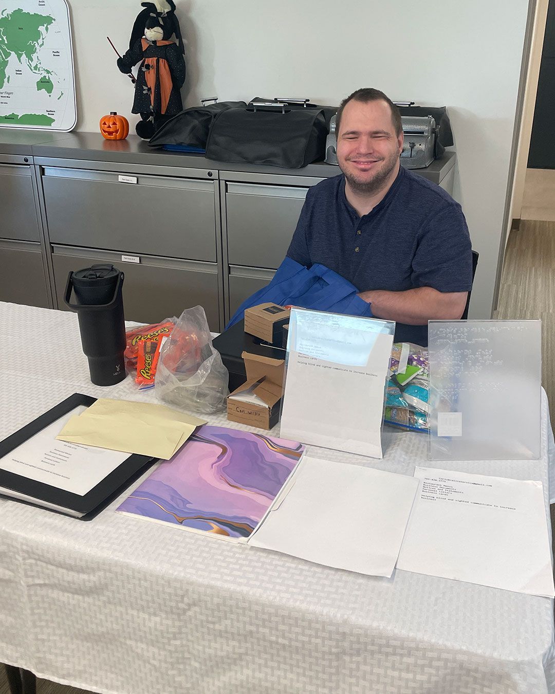 A man representing Cori's Braille Service poses for a photo behind their table at the FRC.