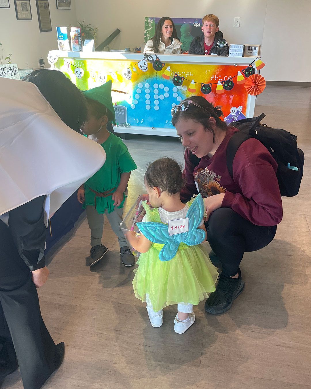 A small girl in a fairy costume inspects her bag of treats while her mother helps.