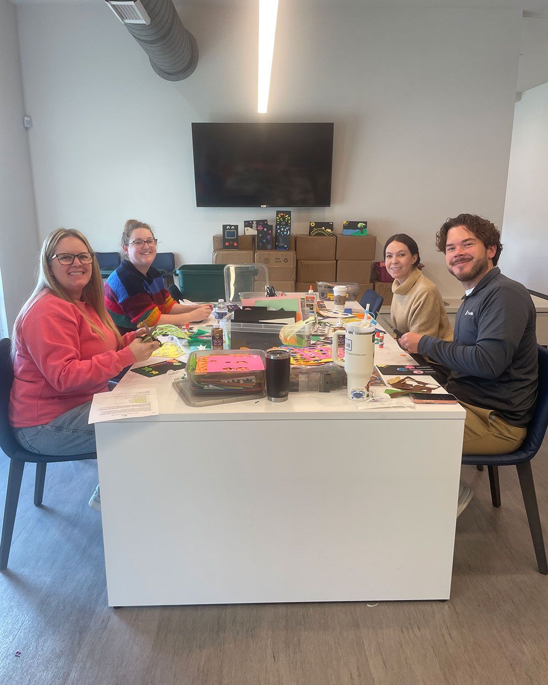 Four volunteers from TWG sit at a the work table in the FRC making birthday cards.