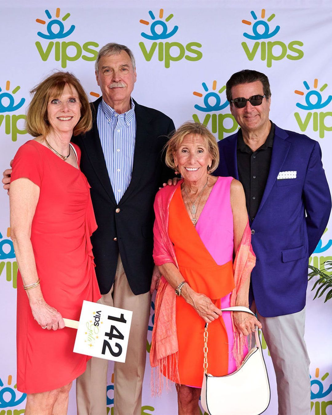 Four people pose for a photo in front of the VIPS step and repeat at the 2025 VIPS Gala.