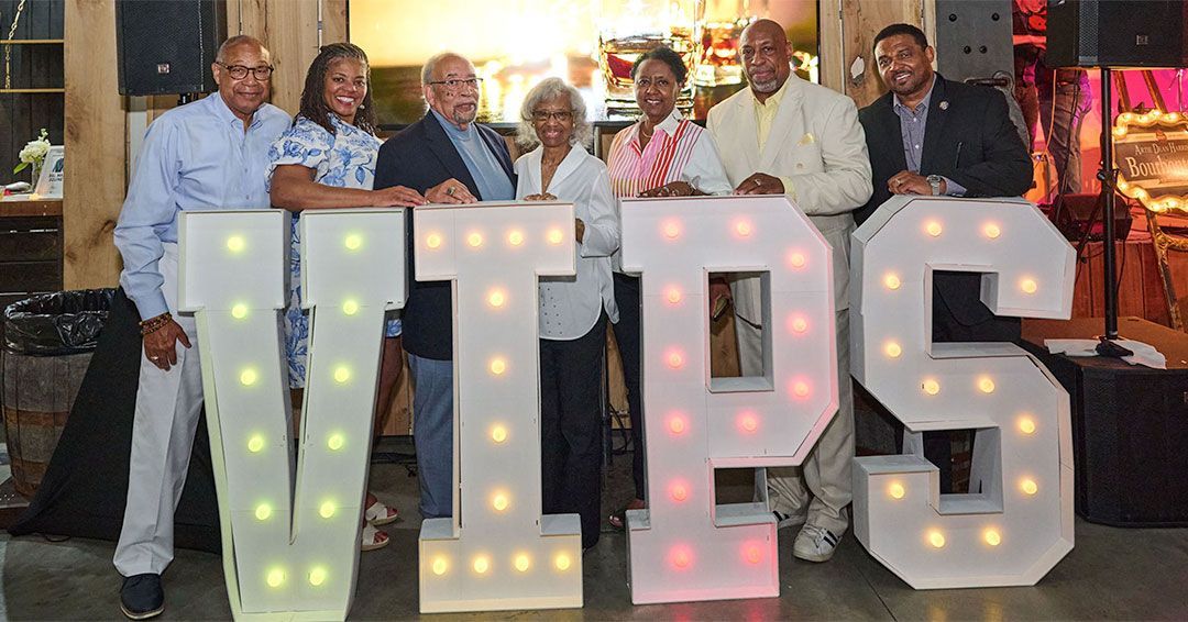 A group of seven poses for a photo in front of giant letters that spell VIPS.