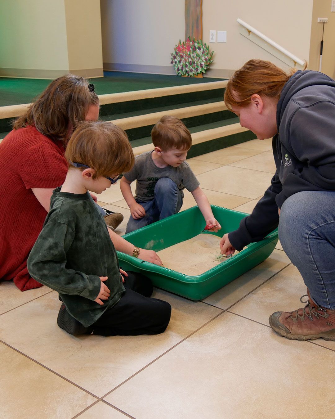Ranger Erin and Ms. Staci play in a sandbox with two small boys.