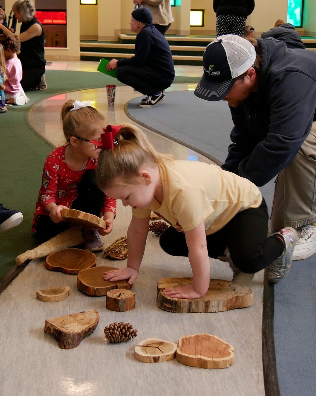 Two small girls play with the pieces of trees, and Ranger Ryan shows them how to count the rings.