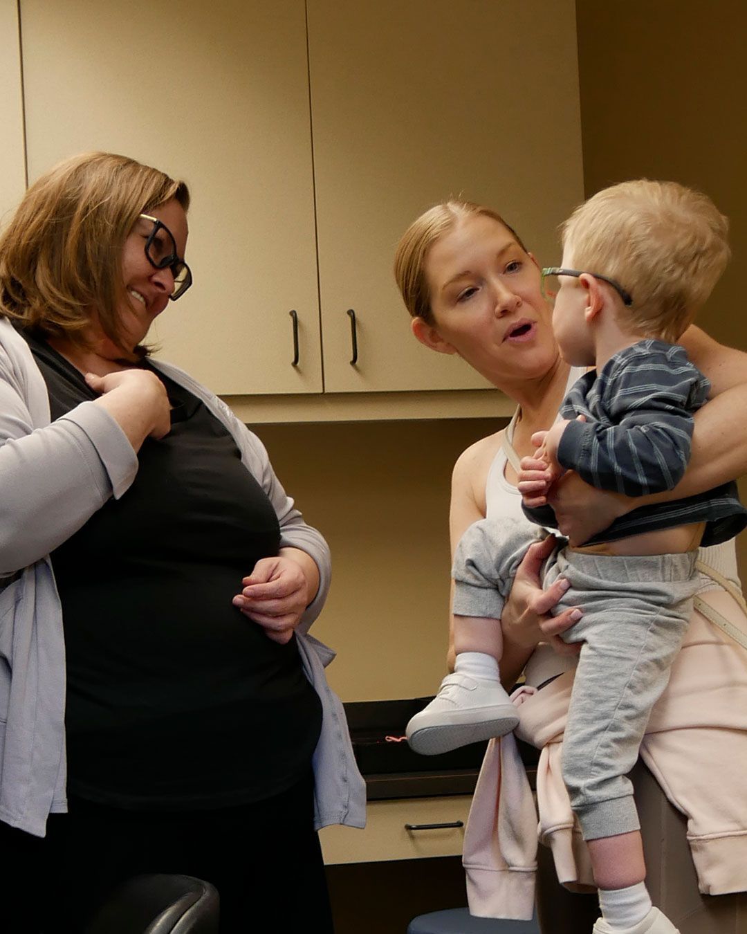 Megan smiles at a small boy, held by his mother, as he tries on a new pair of frames.