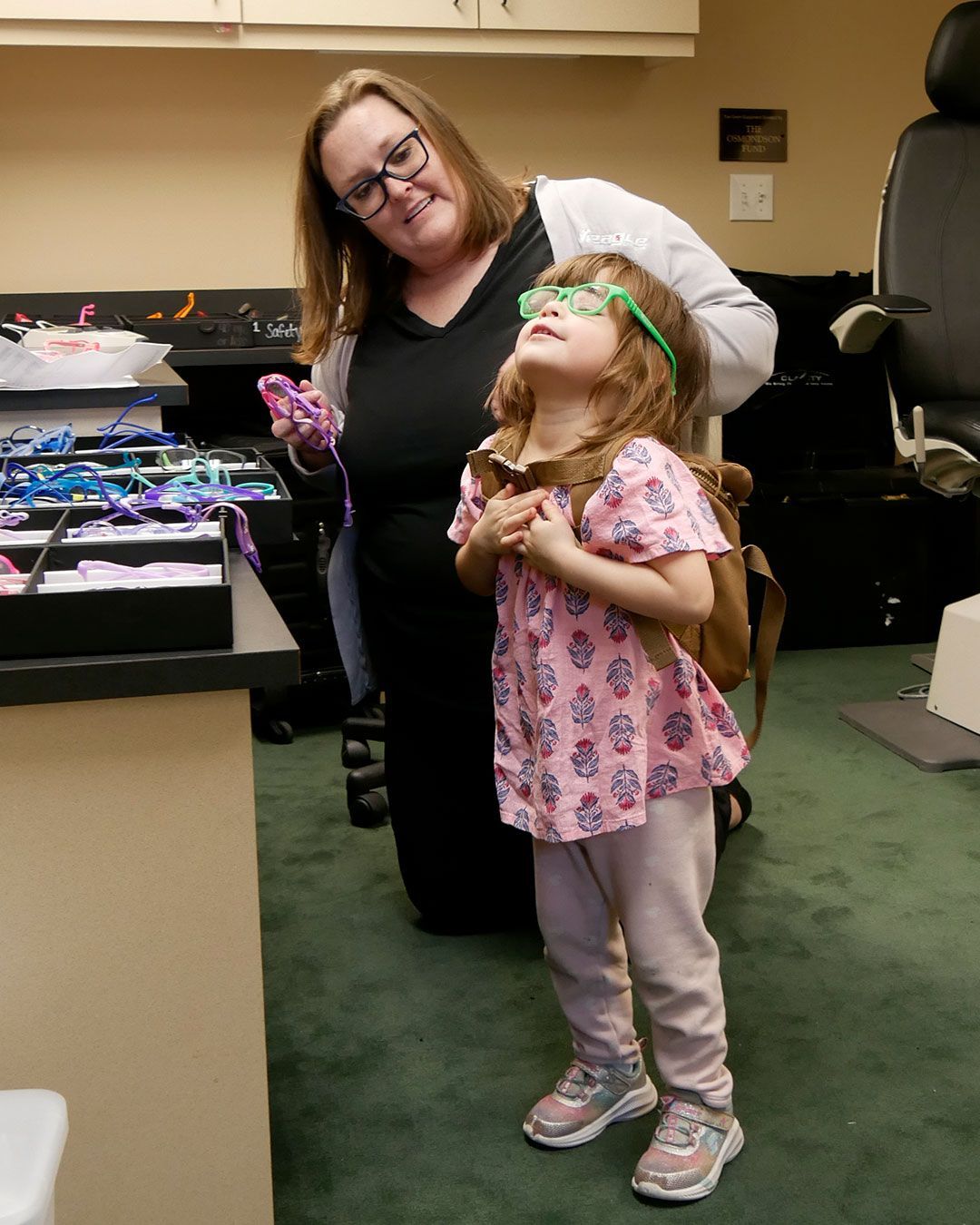 A small girl tries on a pair of green frames.