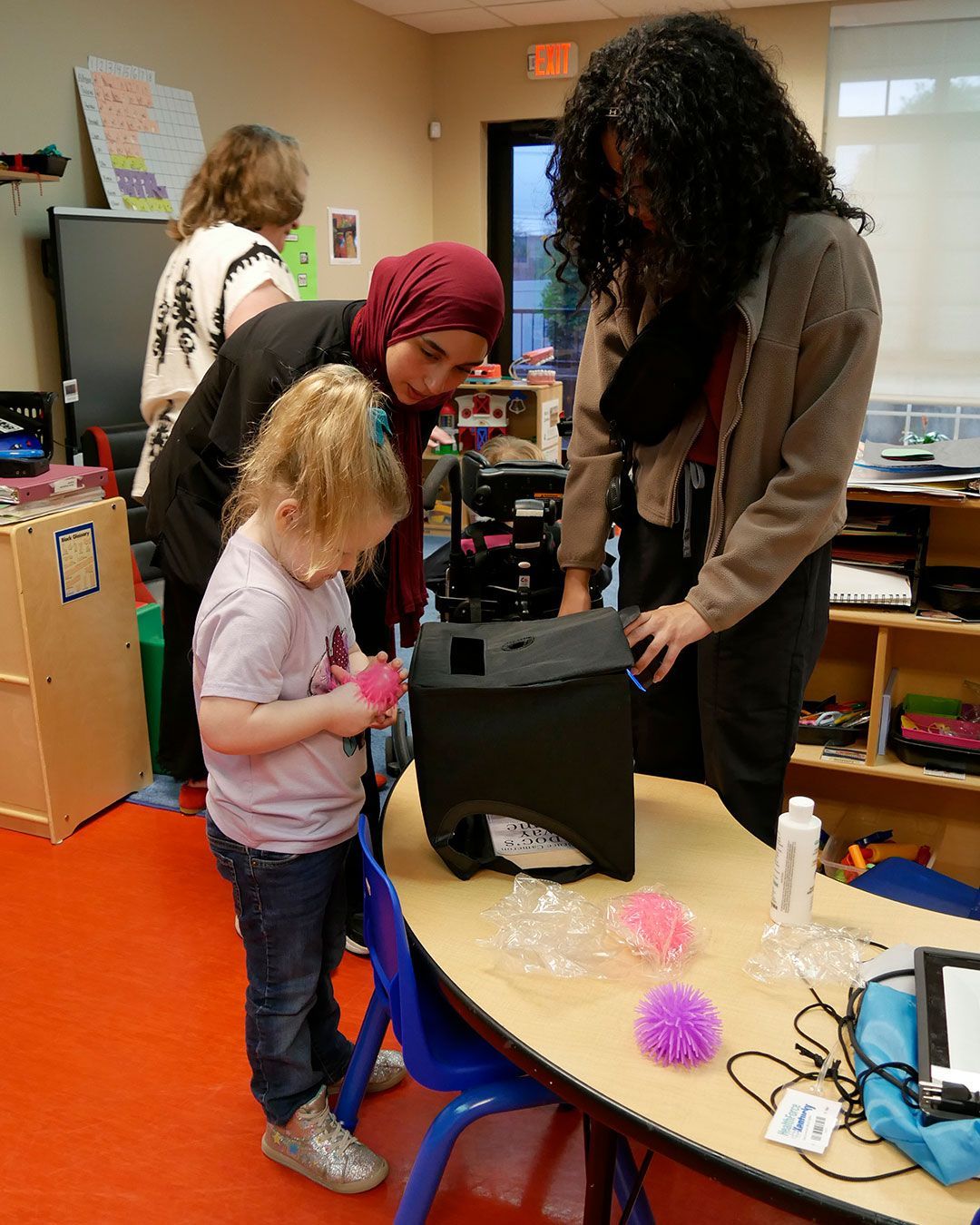 A small girl is about to place her 'germ' in the UV light box with the help of two female physician assistant students.
