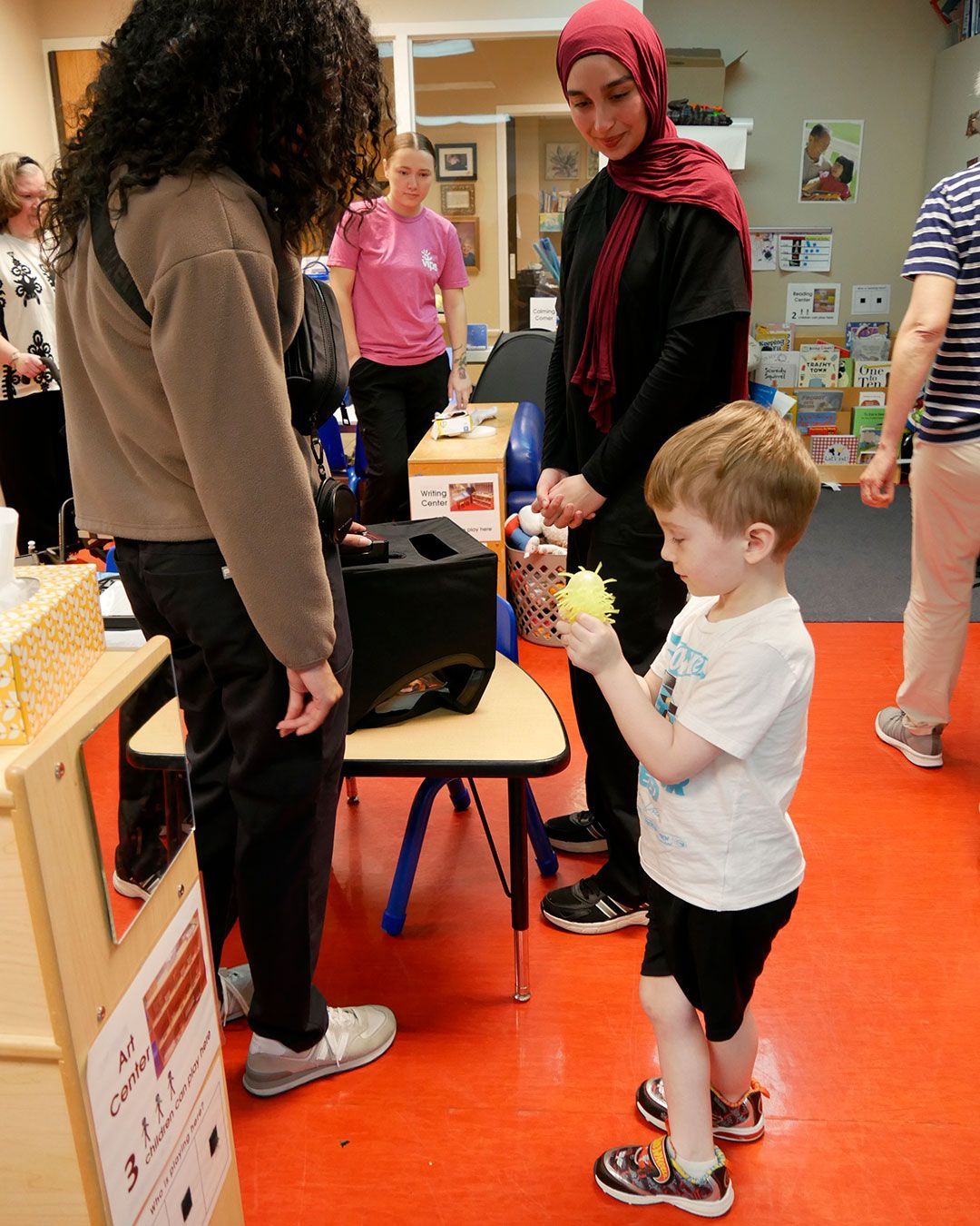 A small boy plays with his new 'germ' toy before placing it in the UV light box with two female physician assistant students watching.